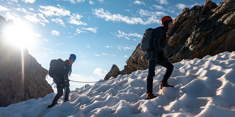 Twee deelnemers van de alpiene c1 cursus lopen aan een touwgroep omhoog in de sneeuw.