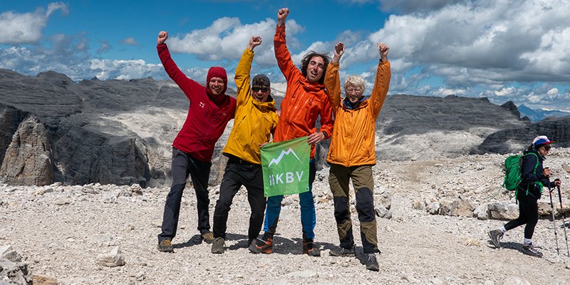 Groep van vier deelnemers aan het juichen met NKBV vlag in hun handen op de top van een berg nadat ze de c3 cursus hebben behaald