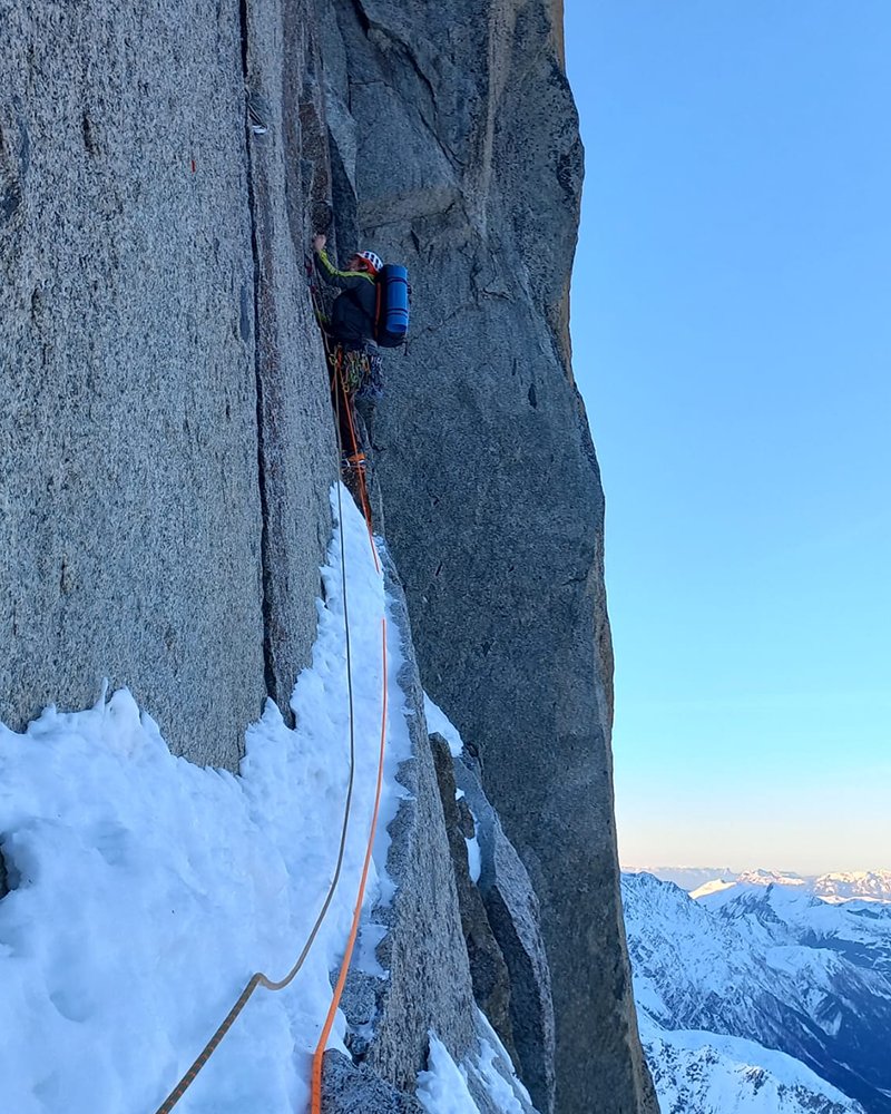 Beklimming Karel Snoek, op grote hoogte aan een touw, langs rotswand met een sneeuw rand