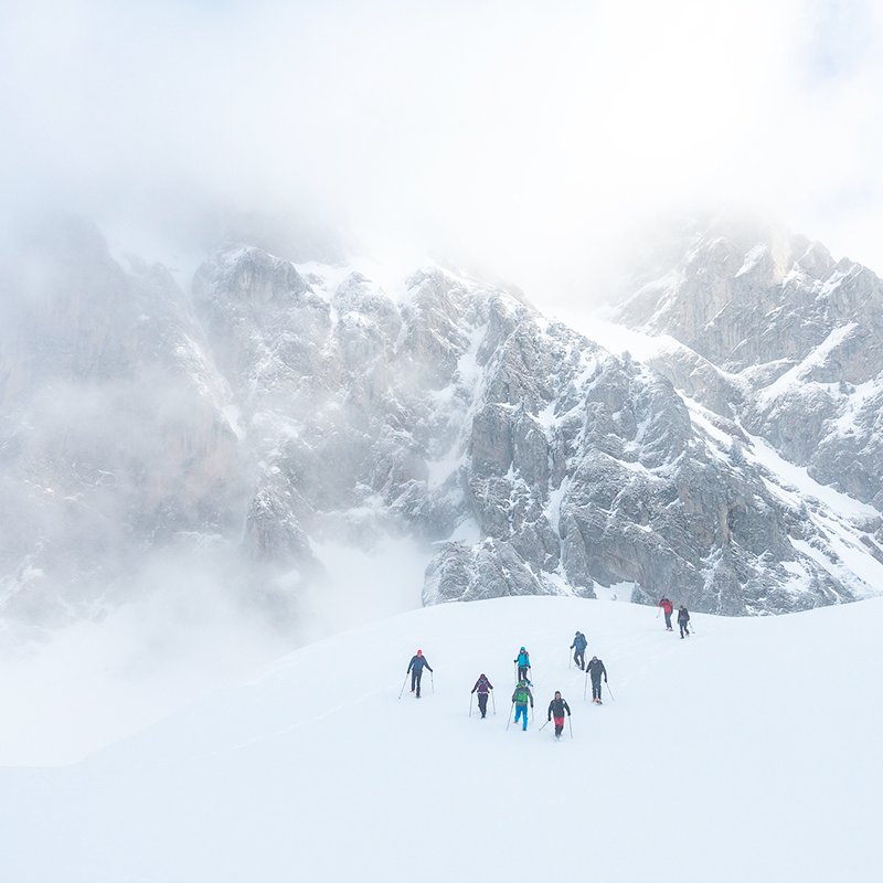 Weidsuitzicht over een besneeuwd berglandschap. Zie 8 sneeuwschoenwandelaars in de verte door een sneeuwveld lopen