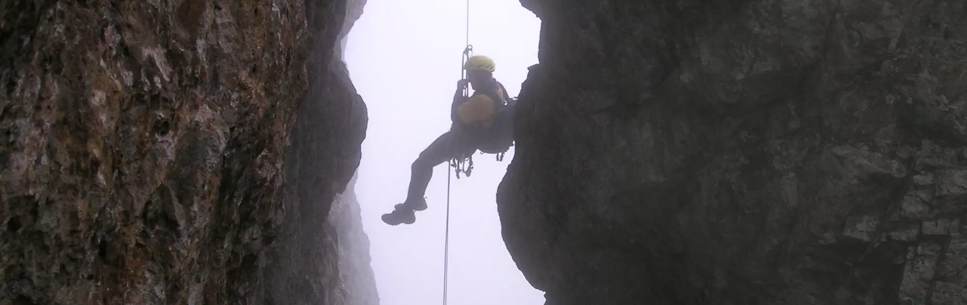 Twee mannen met helmen en outdoor-kleding glimlachen naar de camera. De ene draagt een gele helm en een sjaal met een patroon, terwijl de andere een blauwe helm met een hoofdlamp draagt en een roze to