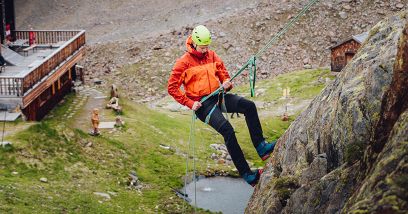 Man in oranje jas is aan het abseilen horizontaal tegen een rotswand