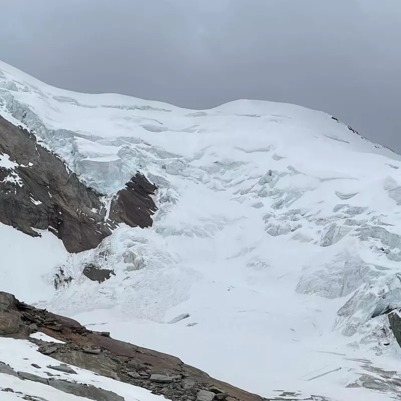 Een met sneeuw bedekte berg met grillige ijsformaties en blootliggende rotspartijen onder een grijze, bewolkte hemel.