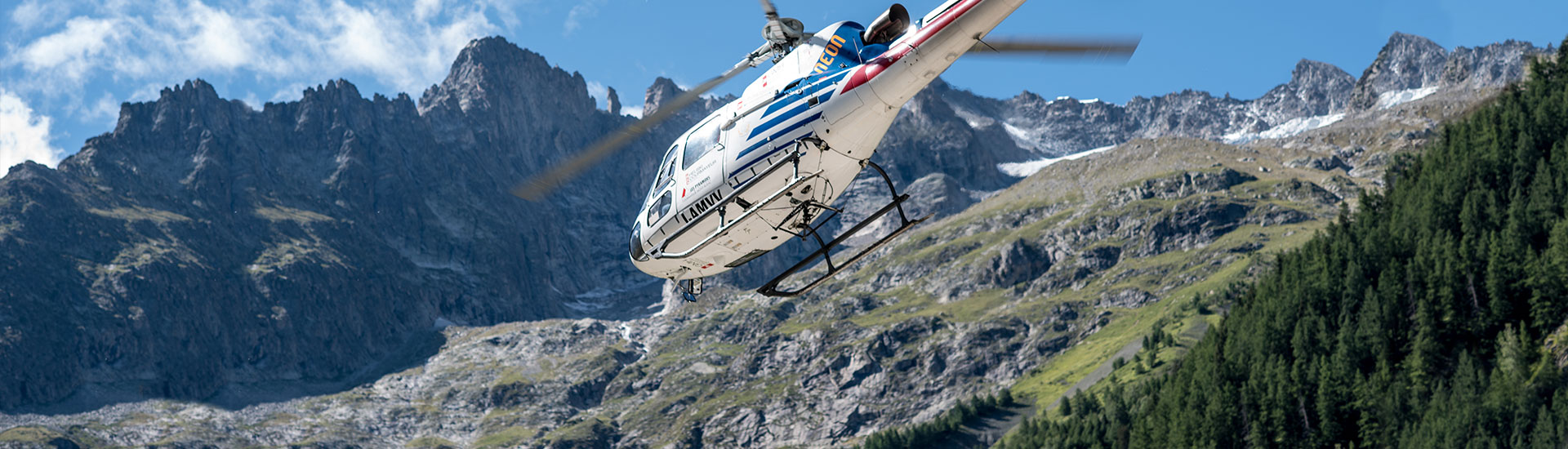 Een helikopter die voor een rotsachtige bergketen vliegt.